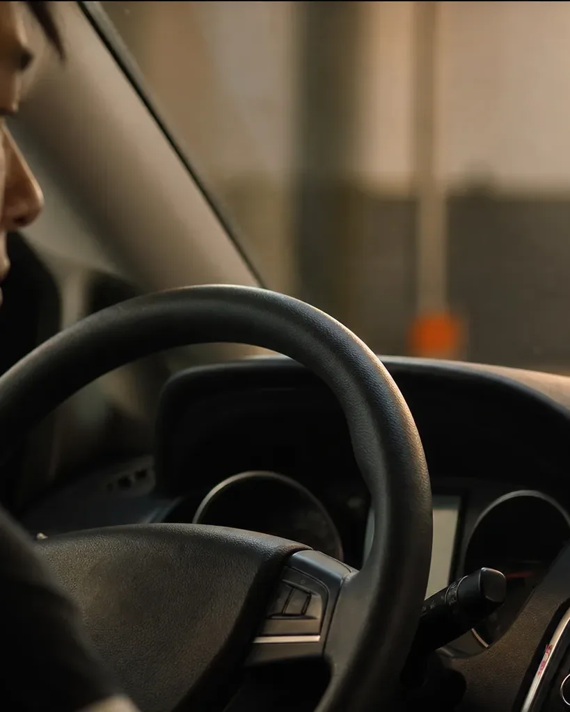 A person sits at the steering wheel of a car, with a phone mounted on the dashboard in a car phone holder